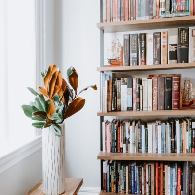 Flowers in vase on bench with talll bookshelf against wall